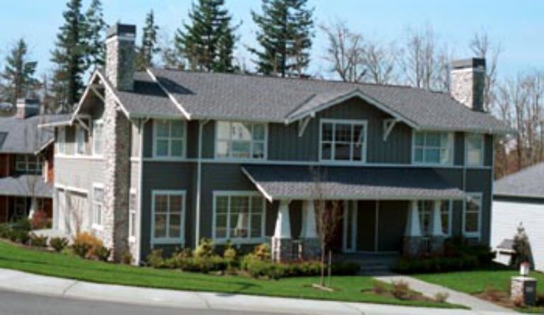  This is a two-story residential house with gray siding, white trim, stonework accents, multiple windows, and a well-manicured lawn on a sunny day. 