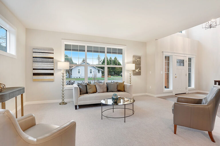 Bright living room with large windows, cream walls, modern furniture, decorative art pieces, and a view of the outside through the glass-paneled door.