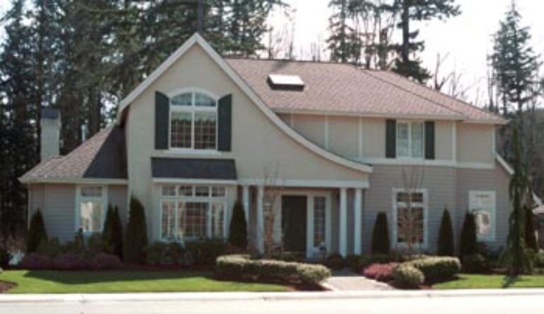 A two-story suburban house with a gabled roof, large front windows, a double garage, and a neatly manicured lawn with shrubs under a clear sky.