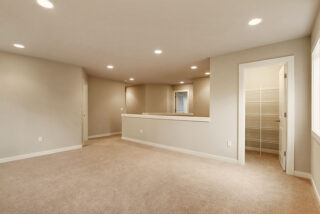 Empty room with beige carpet, neutral walls, recessed lighting, and an open closet with built-in shelves. There's a partial wall with a countertop.