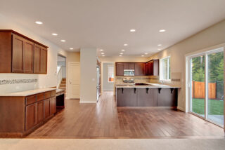 A modern, spacious kitchen with dark wooden cabinets, stainless steel appliances, hardwood floors, and a sliding door leading to a backyard.