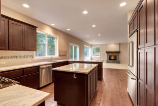 Modern kitchen with dark wood cabinets, stainless steel appliances, granite countertops, and a central island. Recessed lighting and hardwood floors are visible.