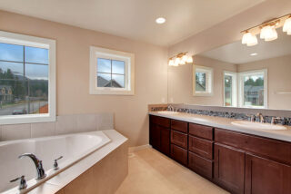 A modern bathroom with a large tub, double vanity with dark cabinets and mirrors, tiled backsplash, and a window with an outdoor view.