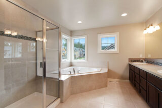 Brightly lit bathroom featuring a glass shower enclosure, large bathtub, tiled floors, double vanity with mirrors, and windows offering an outside view.