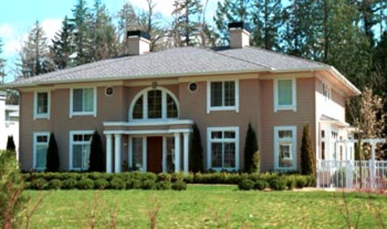 This is an image of a two-story peach-colored house with white columns, large windows, a prominent front entrance, and a green landscaped lawn.