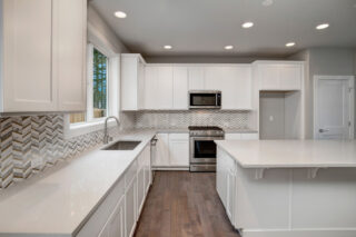 Modern kitchen with white cabinetry, stainless steel appliances, herringbone backsplash, quartz countertops, recessed lighting, and wood flooring. Bright and clean aesthetic.