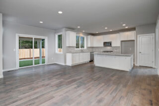 A spacious, modern kitchen with white cabinetry, stainless steel appliances, a center island, hardwood floors, and sliding glass doors leading to a backyard.