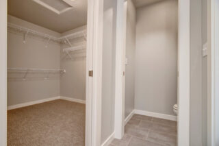 An empty walk-in closet with carpeted flooring and built-in wire shelving, next to a bathroom with tiled floors and a visible toilet.