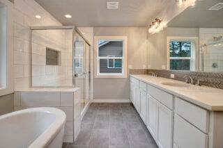 Modern bathroom with a freestanding tub, glass-enclosed shower, double vanity, herringbone backsplash, and large mirror reflecting a window with trees outside.