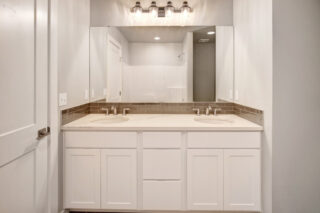 This is a modern bathroom with a double sink vanity, large mirror, tiled backsplash, and a visible shower area with glass doors.