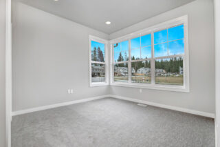 An empty room with grey carpeting, white walls, and a large window allowing ample natural light and providing a view of a suburban landscape.