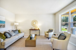 Bright, contemporary living room with neutral tones, two armchairs, a sofa, decorative pillows, large window, artwork, and a circular mirror on the wall.