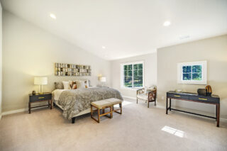 A bright and spacious bedroom with a large bed, two nightstands with lamps, a desk, two benches, and large windows that allow natural light in.