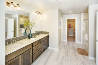 Modern bathroom interior with double vanity sink, large mirror, and walk-in shower, leading to a walk-in closet, decorated with fresh flowers.