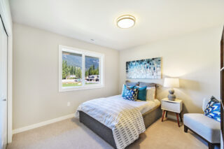 A neatly organized bedroom with a large window offering a mountain view, complemented by patterned bedding and decorative pillows, warm lighting, and modern decor.