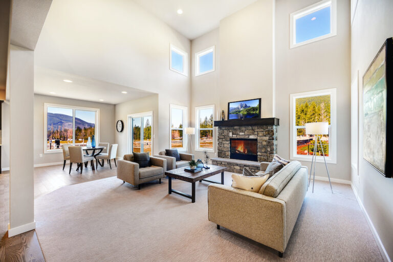 A spacious room with high ceilings, large windows showing a mountain view, a stone fireplace, comfortable seating, and modern decor with ambient lighting.