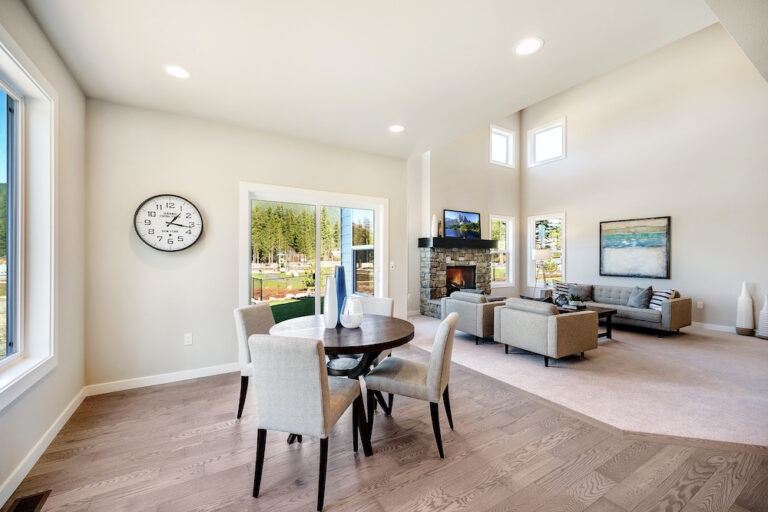 Contemporary living room with high ceilings, large windows, a fireplace, and a connected dining area. Neutral color scheme with wooden floors and modern furniture.