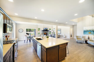 A modern open-concept kitchen with a central island overlooks a dining area and living space with abundant natural light, contemporary furnishings, and hardwood floors.