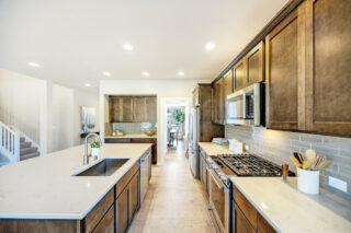 A modern kitchen with dark wood cabinets, stainless steel appliances, white countertops, and a subway tile backsplash. Bright space with wood flooring and recessed lighting.