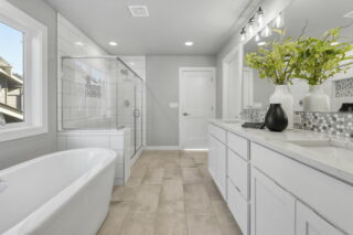 Modern bathroom with a freestanding tub, glass-enclosed shower, double vanity with white cabinets, and decorative vases with greenery on a countertop.