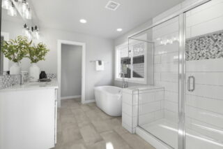 A modern, bright bathroom with a double vanity, large mirror, walk-in shower, freestanding bathtub, and decorative plants. Neutral colors with reflective surfaces dominate.