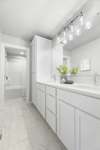 This image shows a modern, white bathroom with marble floor tiles, double vanity, rectangular mirror, and a glass-enclosed shower visible in the background.