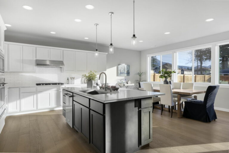 Modern kitchen with white cabinets, stainless steel appliances, central island, pendant lights, and an adjoining dining area with a table and chairs.