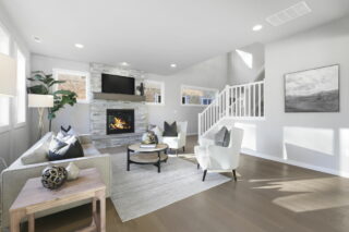 Modern living room with fireplace, television, sofas, coffee table, decorative items, stairway, and artwork under bright natural lighting. Neat, contemporary interior design.