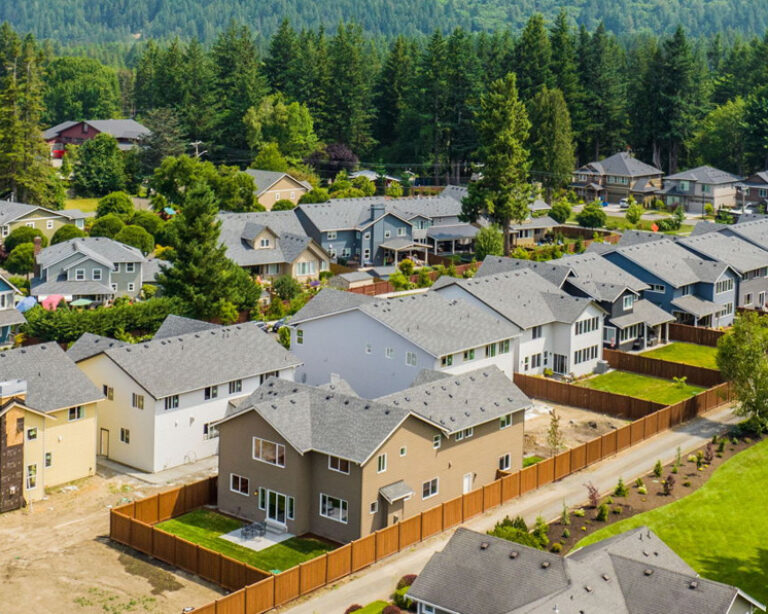 An aerial view of a suburban neighborhood with various houses, some under construction, surrounded by trees under a partly cloudy sky.