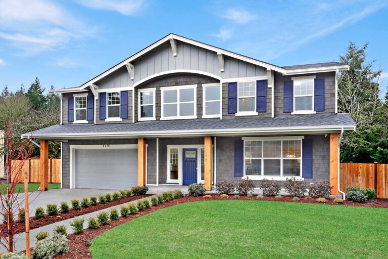 A two-story house with a gray exterior, blue shutters, orange accents, neatly landscaped garden, and a clear blue sky in the background.