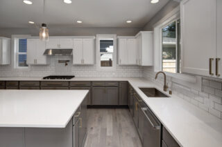 A modern kitchen with white countertops, gray cabinets, subway tile backsplash, stainless steel appliances, and a pendant light over the island.