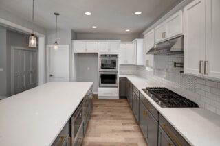 This is a modern kitchen with white countertops, gray cabinets, stainless steel appliances, herringbone backsplash, pendant lights, and wood flooring.