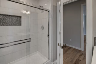 Modern bathroom interior with a glass shower enclosure, white subway tiles, herringbone accent tile, hardwood floors, and neutral wall colors.