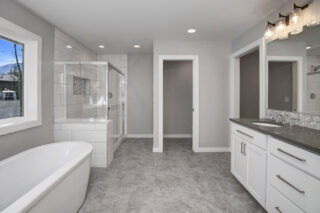 Modern bathroom with a freestanding tub, glass-enclosed shower, double vanity with mirrors, and grey tiled floor. Neutral colors and clean lines throughout.