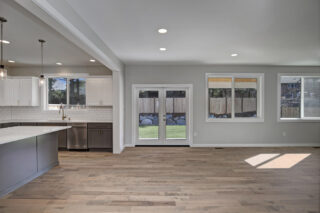 A spacious, modern kitchen with white cabinetry and stainless steel appliances opens to a room with large windows and glass doors leading outside.