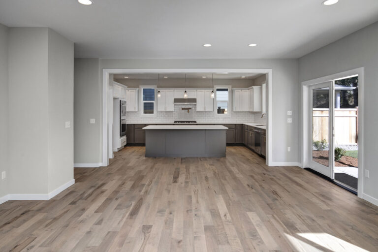 Spacious, modern kitchen with white cabinetry, gray island, stainless steel appliances, hardwood floors, and sliding glass doors leading to a backyard.