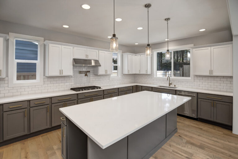 Modern kitchen with white countertops, two-tone cabinets, stainless steel appliances, subway tile backsplash, pendant lights, and hardwood floors. No people present.