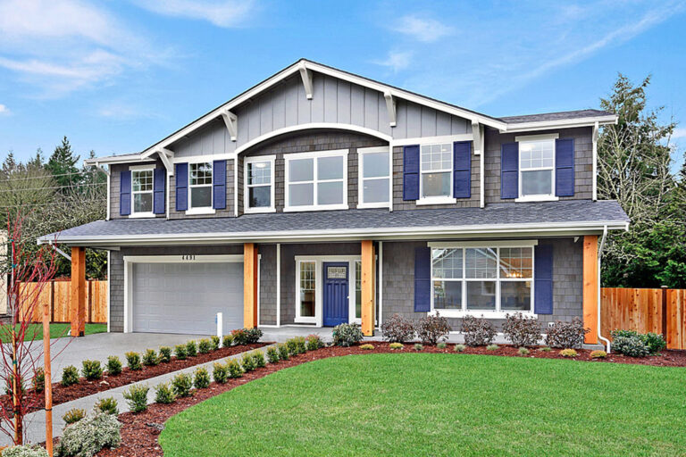  Two-story suburban house with gray siding, blue shutters, white garage door, landscaped front yard, and a partly cloudy sky above. 