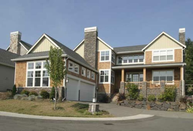 This image shows a large two-story house with a mix of stone and wooden siding, featuring a prominent garage, balconies, and a clear sky above.