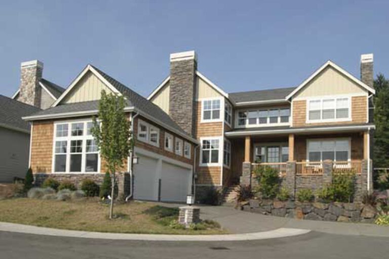 This image shows a large two-story house with a mix of stone and wooden siding, featuring a prominent garage, balconies, and a clear sky above.