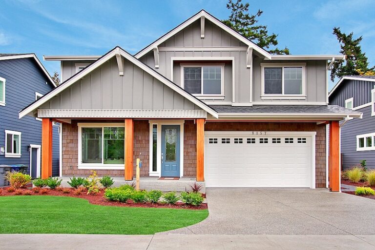  A modern two-story house with gray siding, white trim, orange pillars, a double garage, and neatly landscaped yard under a cloudy sky. 