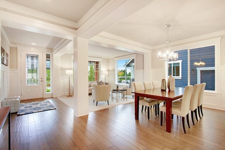 This is an elegant dining room with a wooden table, white chairs, and a chandelier, leading into a living area with a fireplace and seating.