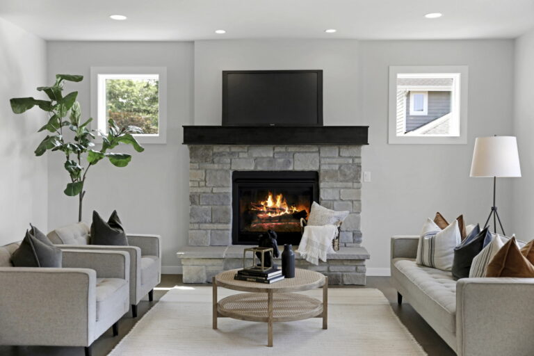 A modern living room with a stone fireplace, TV, two sofas, decorative pillows, a floor lamp, a coffee table, and a large leafy plant.