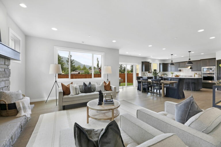 A modern open-concept living space with a kitchen, dining area, and living room. Neutral tones, contemporary design, well-lit with natural and recessed lighting.