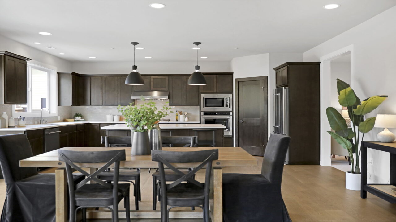 Modern kitchen with dark wood cabinets, stainless steel appliances, an island, pendant lights, and a dining area with a wooden table and chairs.